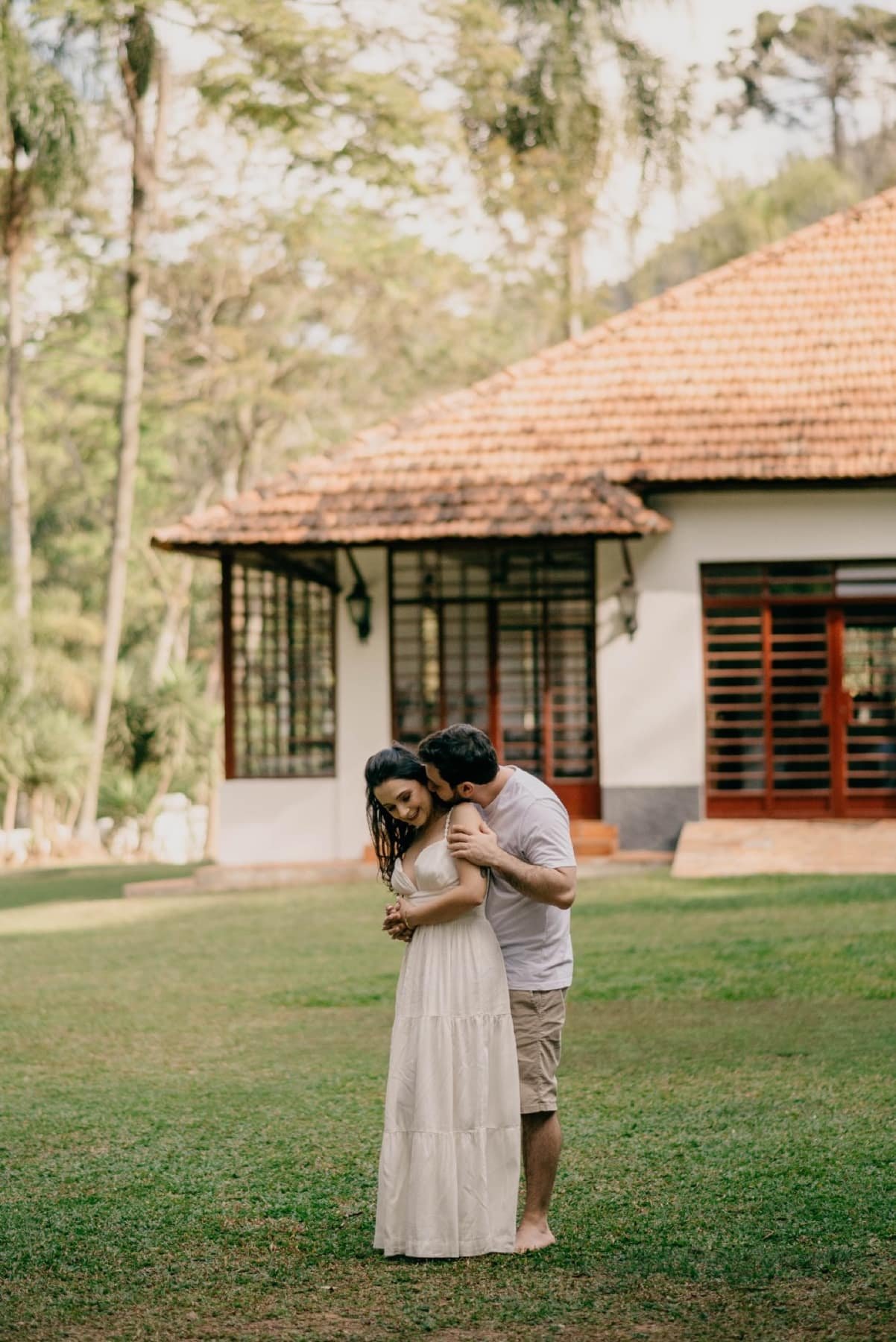 Casal abraçado no gramado em frente ao casarão