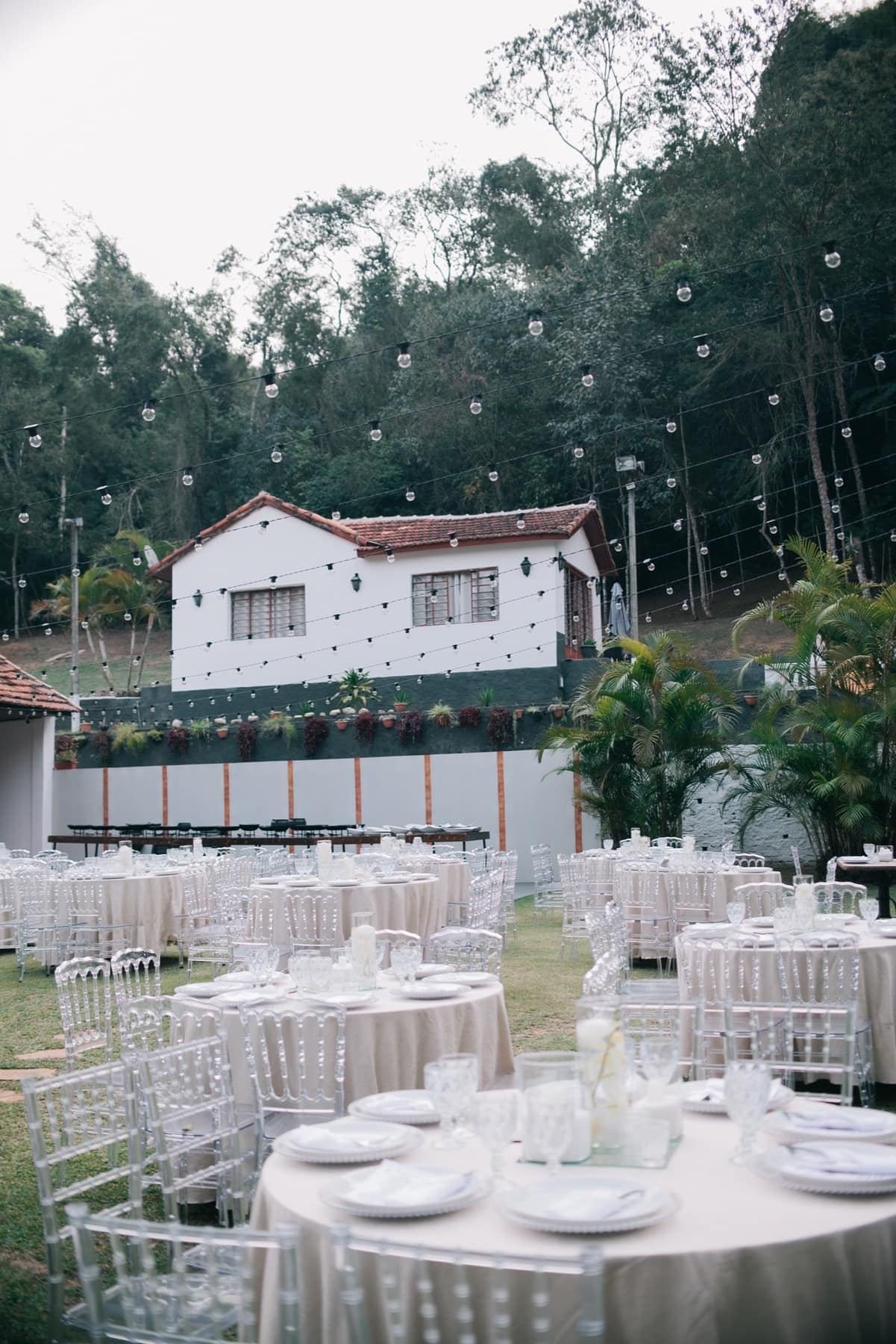 Recepção no jardim com luzes suspensas e mesas redondas